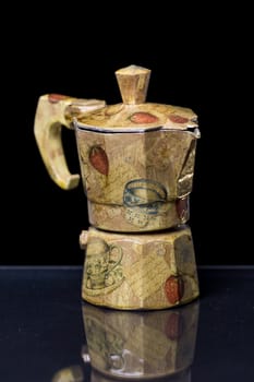 A decorated Moka italian coffee machine with fruit and vintage handcrafted decoupage work on a reflective black surface with black background