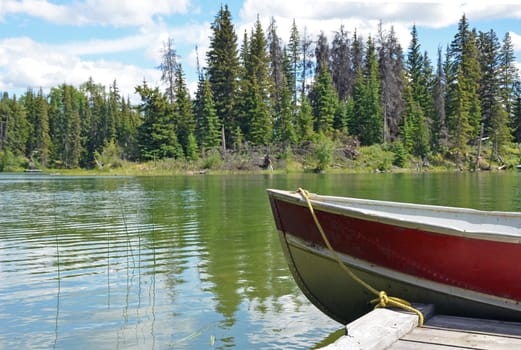 Old red boat tied to wooden dock on lake