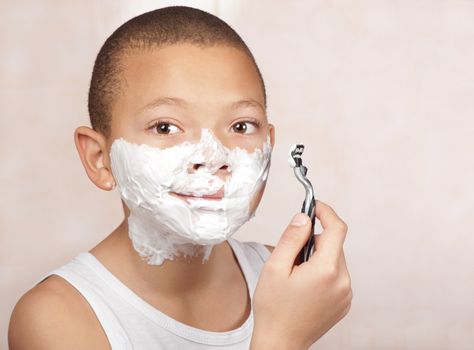 A young boy with no beard experiments with his father's shaving utensils.