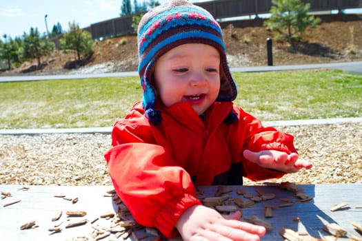 A one-year-old boy plays at a park outdoors with wood chips and structures to keep him entertained.