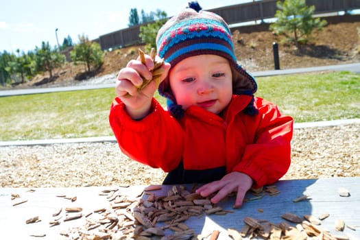 A one-year-old boy plays at a park outdoors with wood chips and structures to keep him entertained.