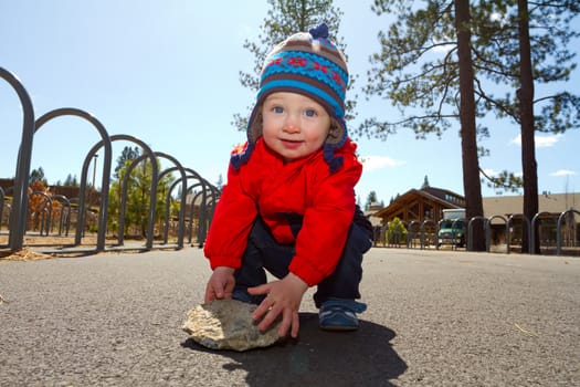 A one-year-old boy plays at a park outdoors with wood chips and structures to keep him entertained.