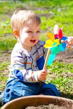 A one year old boy plays with a whirligig propeller pinwheel outside while wearing a striped shirt.