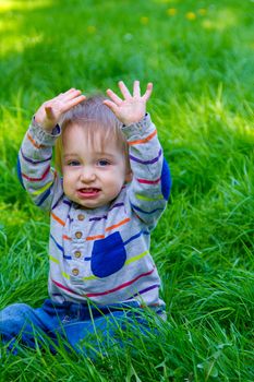 A one year old toddler boy plays in the grass in his backyard while waving and looking cute and smiling.