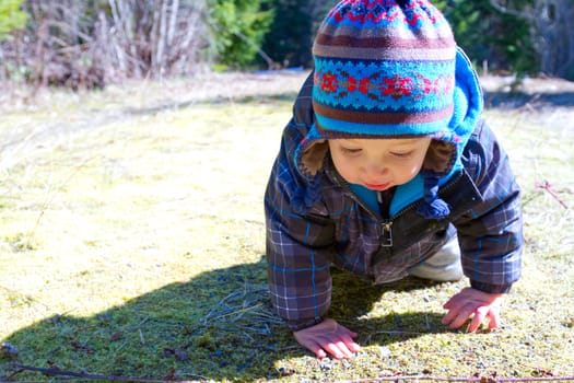 A young boy wears a jacket and warm hat while hiking in the cold near snow in the winter and having fun exploring.