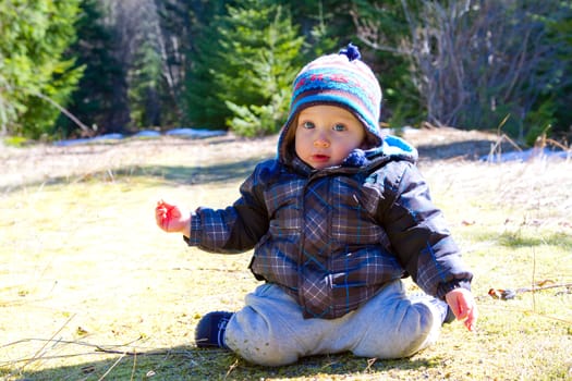 A young boy wears a jacket and warm hat while hiking in the cold near snow in the winter and having fun exploring.
