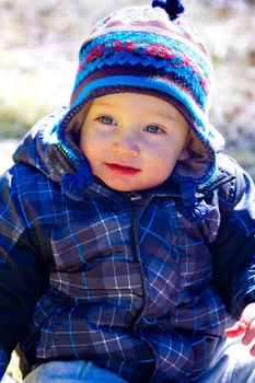 A young boy wears a jacket and warm hat while hiking in the cold near snow in the winter and having fun exploring.