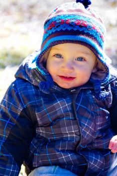 A young boy wears a jacket and warm hat while hiking in the cold near snow in the winter and having fun exploring.