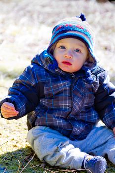 A young boy wears a jacket and warm hat while hiking in the cold near snow in the winter and having fun exploring.