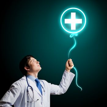 Young male doctor holding balloon with medical sign