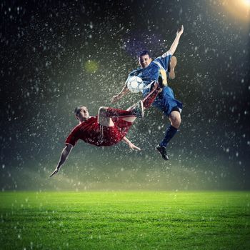 two football players in jump to strike the ball at the stadium