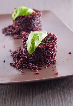 Black rice type "Venere" over brown plate with basil leaf
