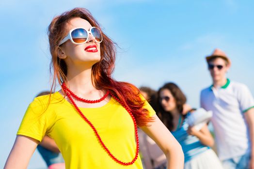 stylish young woman in sunglasses on the background of blue sky and friends