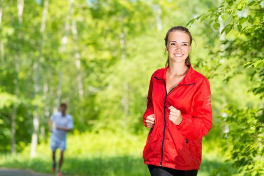 healthy young female athlete running in a summer park smiling and happy while working out