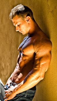 Attractive and muscular male bodybuilder leaning against yellow wall looking down