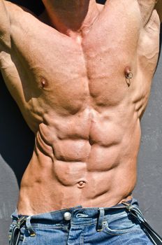 Bodybuilder torso with arms up, ripped abs and pecs with nipple piercing, wearing jeans