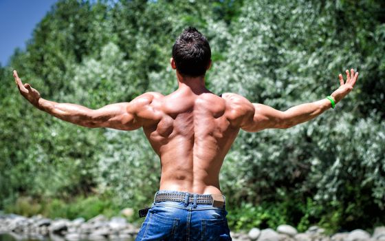 Muscle man in jeans, outdoor with arms spread open, seen from the back, muscular shoulders
