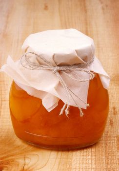 Glass Jar with Homemade Apricot Jam Covered Butter-Paper on Wooden background