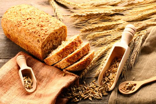 Rye spikelets and sliced bread on wooden background