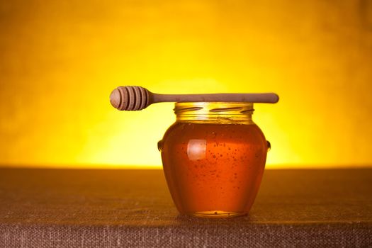 Honey jar with dipper over yellow background   