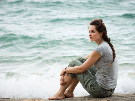 A sad and pensive woman sitting by the ocean deep in thought.