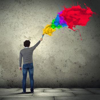 Young man spraying colour paints over background