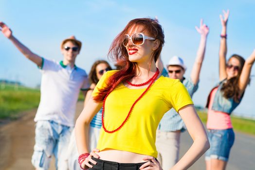 stylish young woman in sunglasses on the background of blue sky and friends