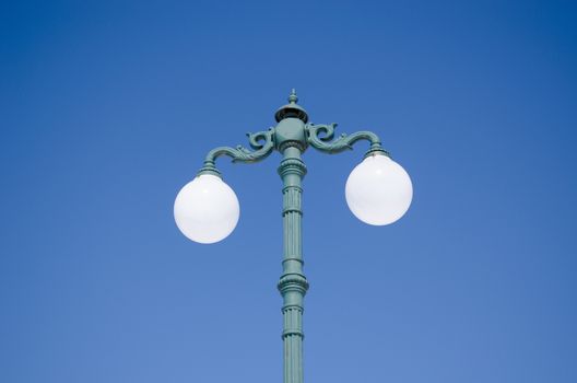 vintage lighting pole with double twin round glass lamps on background of blue sky.