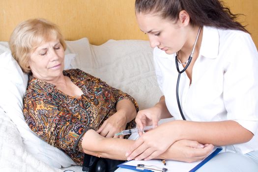 A young woman doctor puts a shot of an elderly patient