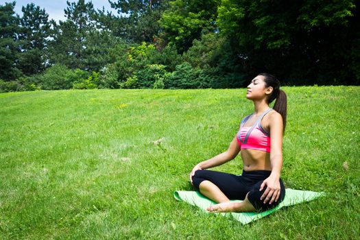 Young fit woman practices yoga in the park to meditate and relax