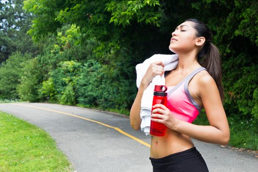 Young woman resting with towel and water bottle after running