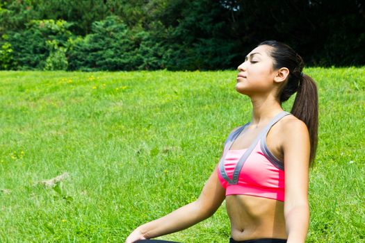 Young fit woman practices yoga in the park to meditate and relax