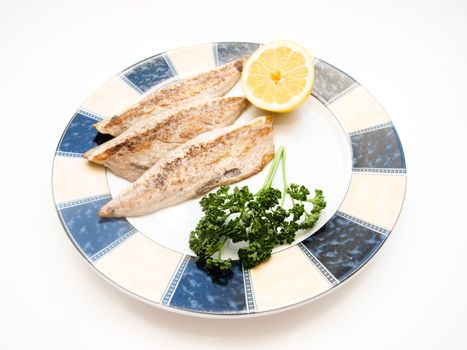 Fried filet of mackerel fish on colored plate with half a lemon and parsley