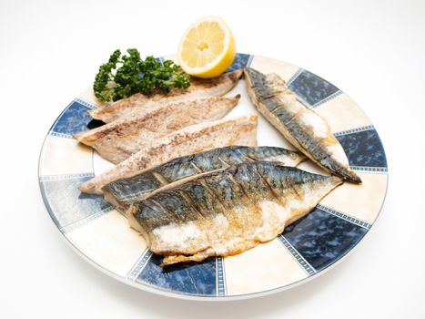 Fried filet of mackerel fish on colored plate with half a lemon and parsley