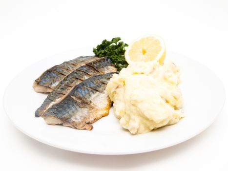 Fried mackerel fish filet with mashed potatoes, half a lemon and parsley, on white plate towards white