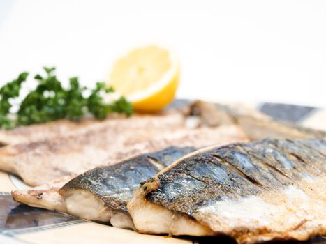 Fried filet of mackerel fish on colored plate with half a lemon and parsley