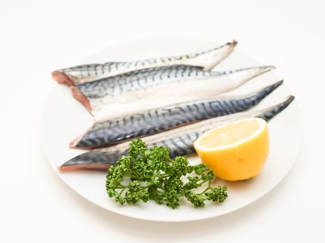 Raw mackerel fish filet with half a lemon and parsley on white plate