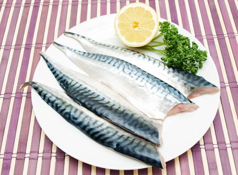 Raw mackerel fish filet with half a lemon and parsley on white plate on purple wooden table cover