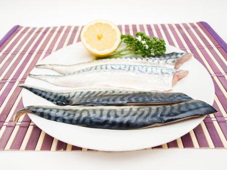 Raw mackerel fish filet with half a lemon and parsley on white plate on purple wooden table cover