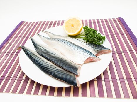 Raw mackerel fish filet with half a lemon and parsley on white plate on purple wooden table cover