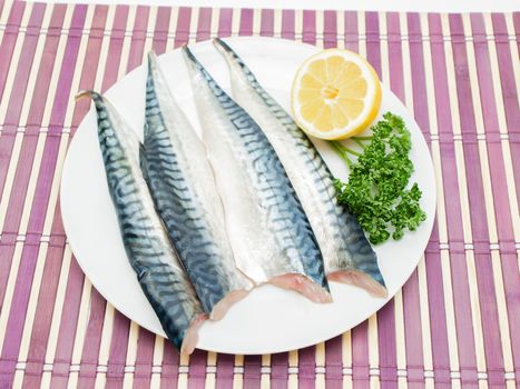 Raw mackerel fish filet with half a lemon and parsley on white plate on purple wooden table cover