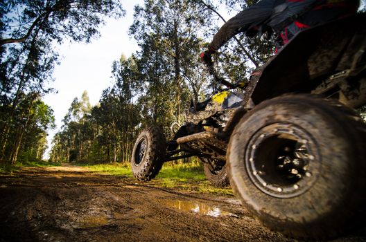 Quad rider jumping on a muddy forest trail.