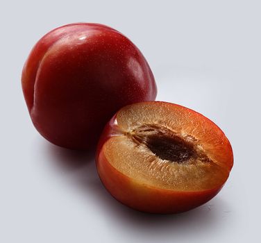 Whiole and half of red plums on the grey background
