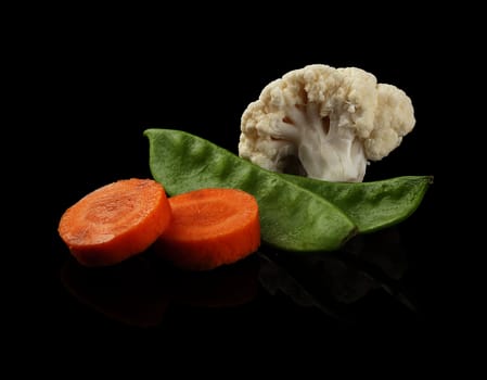 Fresh carrot, green peas and cauliflower on the black background