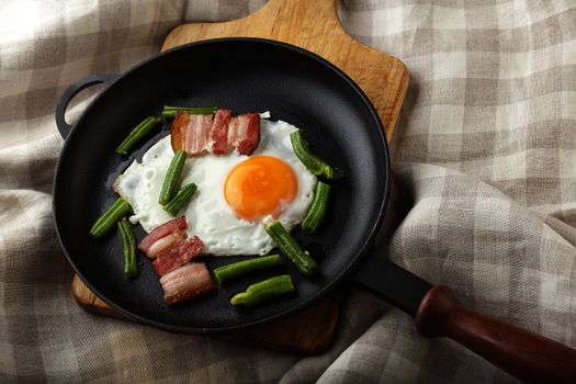 Fried egg with bacon and string bean on the black pan