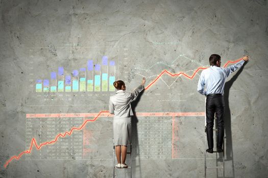 businesspeople standing on ladder drawing diagrams and graphs on wall