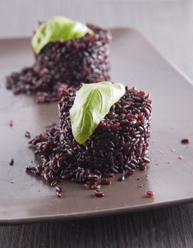 Black rice type "Venere" over brown plate with basil leaf