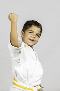 A young boy punching up dressed in a karate uniform.