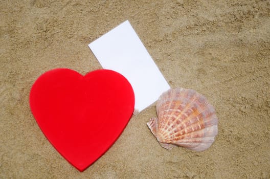 Red Heart shape, big seashell and piece of paper on the beach