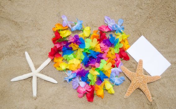Heart shape of the Hawaiian flowers, two starfishes and piece of paper on sandy beach